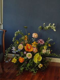 a vase filled with lots of flowers on top of a wooden floor next to a blue wall