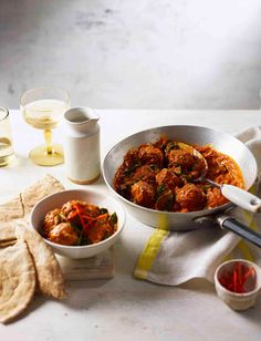 a table topped with two bowls filled with meatballs and veggies next to wine glasses