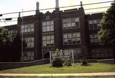 an old brick building with lots of windows on the top floor and some bushes in front of it