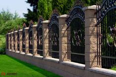 a row of wrought iron gates on the side of a stone wall with green grass