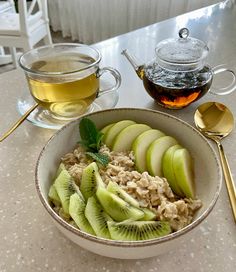 a bowl of oatmeal with kiwi slices and sliced apples next to a cup of tea