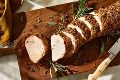 sliced pork with herbs and seasoning on a wooden cutting board next to a knife