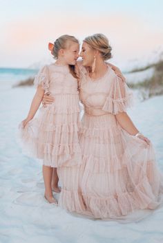 two women in pink dresses standing on the beach