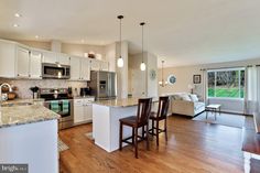 an open kitchen and living room area with hardwood floors, white cabinetry, stainless steel appliances and large windows