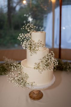 a three tiered cake with baby's breath on top sitting on a table