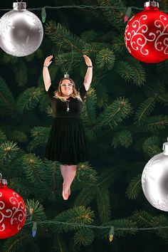 a woman in a black dress is suspended by christmas ornaments