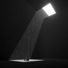 a person sitting on the ground in front of a wall with a light coming from it