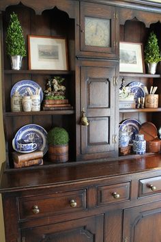 an old wooden cabinet with blue and white plates on the top, along with potted plants