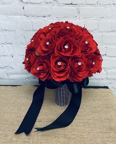 a bouquet of red roses and pearls on a burlock with black ribbon in front of a white brick wall