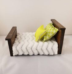 a small wooden bed with two pillows on top of it and a white blanket behind it