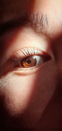 an orange eye with long lashes is seen through the shadow of someone's face