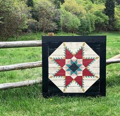 a wooden fence with a patchwork quilt on it's side in the grass