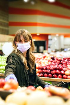 a woman wearing a face mask while standing in front of produce at a grocery store