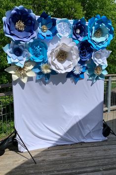 a white and blue backdrop with paper flowers on the top, sitting on a wooden deck