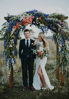 a man and woman are standing under an arch made out of branches with flowers on it