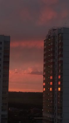 the sun is setting behind two tall buildings in front of a red sky with clouds