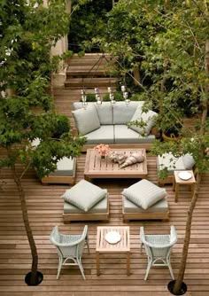 an outdoor patio with furniture and trees on the deck, in front of a wooden fence