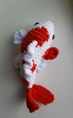 an orange and white knitted fish laying on the ground