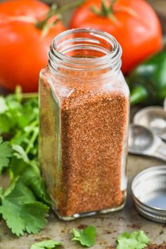 a jar filled with seasoning next to spoons and tomatoes