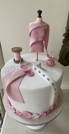 a white cake with pink decorations and sewing supplies on it's top, sitting on a table next to a mirror