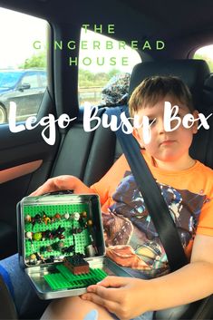 a young boy sitting in the back seat of a car holding a lego box