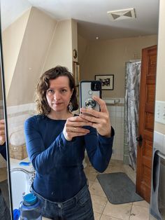 a woman taking a selfie in front of a bathroom mirror with her cell phone