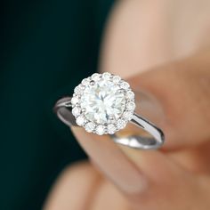 a woman's hand holding an engagement ring with a white diamond center stone in the middle