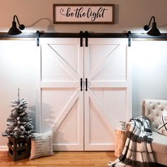 a white barn door with the words be the light above it and a christmas tree next to it