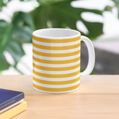 a yellow and white striped mug sitting on top of a table next to a book