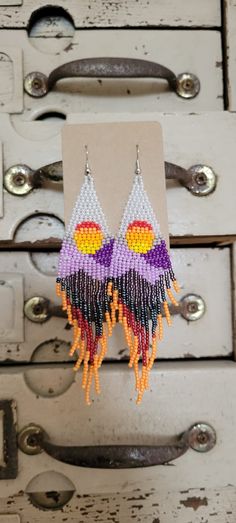 two pairs of colorful beaded earrings hanging from hooks on a wooden cabinet door with metal handles