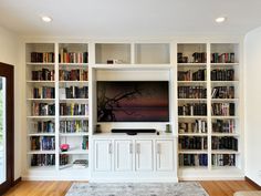 a living room with white bookcases and a flat screen tv on the wall