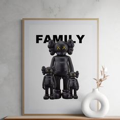 an art print with the word family on it in front of a white vase and wooden shelf