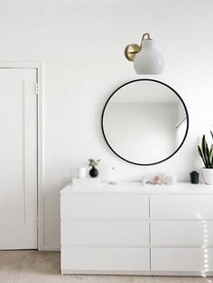 a white bathroom with a round mirror on the wall and plants in pots next to it