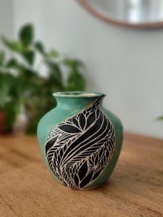 a green vase sitting on top of a wooden table next to a potted plant