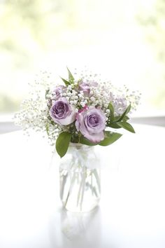 a vase filled with purple roses and baby's breath on top of a table