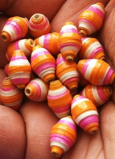 a hand holding a bunch of small orange and pink striped beads