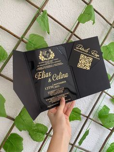 a person holding up a black and gold wedding card