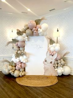 a white sign surrounded by balloons and greenery in a room with wooden flooring