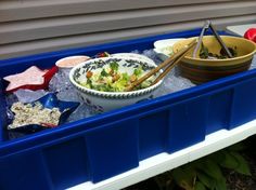 a plastic container filled with food and chopsticks next to a bowl full of salad