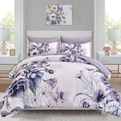 a bed with purple flowers on it and two nightstands in front of the window