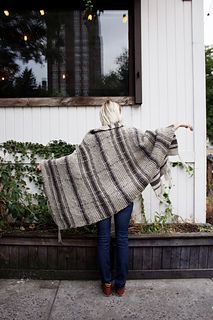 a woman is standing on the sidewalk wearing a blanket