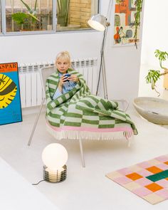 a little boy sitting in a chair under a green and white blanket while looking at his cell phone