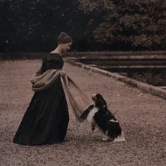 a woman in black dress holding a pink umbrella next to a dog on gravel road