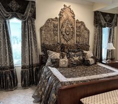 a large bed sitting in a bedroom next to two windows with drapes on them