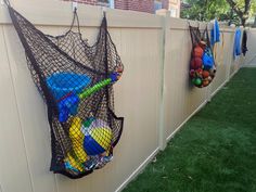 there are many balls in the net hanging on the fence wall and behind it is a stuffed animal