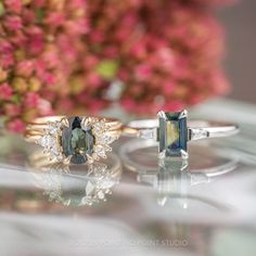 two engagement rings sitting on top of a table with flowers in the backgroud