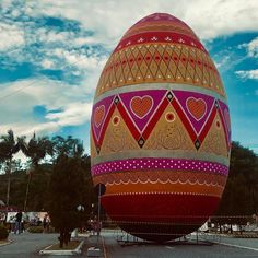 an easter egg is sitting in the middle of a parking lot with people walking around it