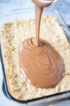 a chocolate sauce being poured on top of a cookie crust in a baking dish with a spatula