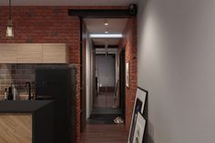 a narrow hallway with brick walls and wood flooring on the other side, leading to an open kitchen area