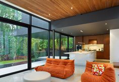 an orange couch and two chairs in a room with large glass windows looking out onto the backyard